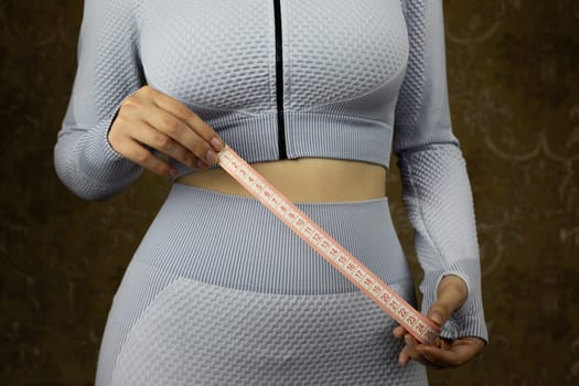 Sport girl in tight fitting suit holds measuring tape in her hands to measure her waist, concept of sports and healthy lifestyle