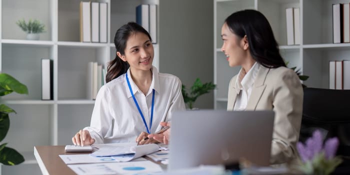 Two businesswomen engaged in a teamwork planning and analysis discussion in a modern office environment.