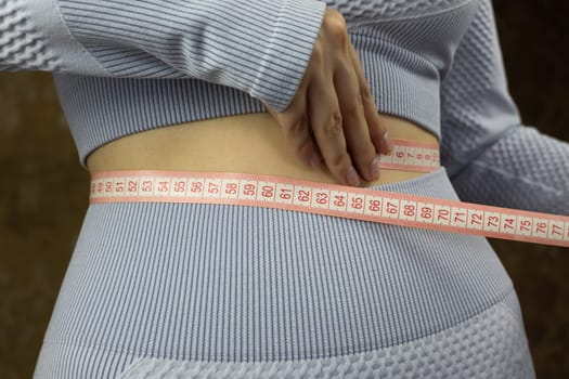 Close up of girl in gym suit measuring the waist with special flexible tape, thin girl with narrow waist measures indicators, sports and healthy life