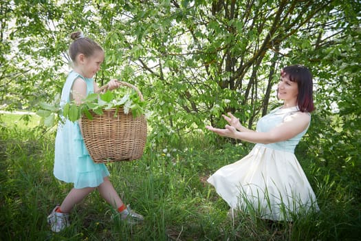 Happy mother and daughter enjoying rest, playing and fun on nature on a green lawn and with blooming apple tree in the background. Woman and girl resting outdoors in summer and spring day