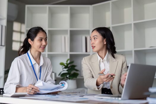 Two businesswomen engaged in teamwork, planning, and analysis discussion in a modern office environment.