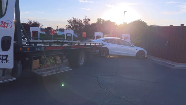 Santa Fe, New Mexico, USA-June 10, 2024-Slow motion-A Tesla electric vehicle is being delivered by a tow truck to a Tesla Supercharger station after running out of charge. The scene captures the car being carefully handled by a worker, who is preparing to connect it for recharging. The Supercharger station is situated in a well-maintained area, with several other charging units visible in the background, indicating a dedicated facility for electric vehicle charging. The image highlights the support and infrastructure available for electric vehicle owners, ensuring they can continue their journey with minimal disruption.