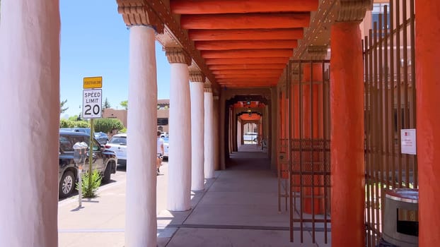 Santa Fe, New Mexico, USA-June 11, 2024-Slow motion-A picturesque covered walkway in Santa Fe, New Mexico, featuring traditional adobe architecture and vibrant blue window frames. The pathway is lined with shops, including a silversmith, showcasing the city rich cultural heritage and lively atmosphere. Potted plants add a touch of greenery to this charming scene.