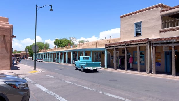Santa Fe, New Mexico, USA-June 11, 2024-Slow motion-A vintage blue pickup truck drives through a historic downtown area, showcasing charming adobe buildings and a vibrant atmosphere on a sunny day.