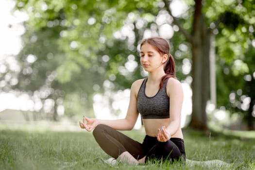 Young Girl In Lotus Pose Practices Yoga On Grass