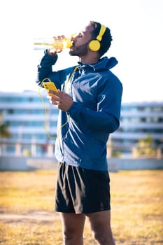 Athletic man with yellow headphones drinking water while working out.