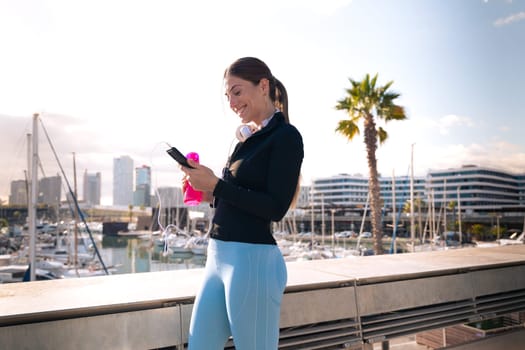 Cheerful girl using an app on a cell phone and holding a sports bottle.