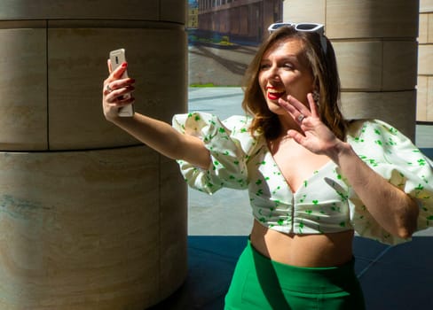 Joyful young caucasian woman winks, bites her tongue, takes selfie on phone. Blonde model wears hat in sunny weather. Positive emotions concept. High quality photo