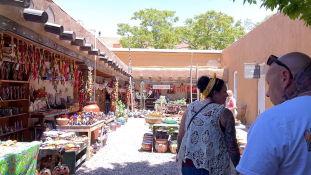 Santa Fe, New Mexico, USA-June 11, 2024-Slow motion-A vibrant outdoor market showcasing an array of colorful ceramics, pottery, and handcrafted items. Shoppers explore the unique local crafts under a sunny sky, surrounded by traditional adobe architecture.