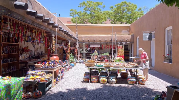 Santa Fe, New Mexico, USA-June 11, 2024-Slow motion-A vibrant outdoor market showcasing an array of colorful ceramics, pottery, and handcrafted items. Shoppers explore the unique local crafts under a sunny sky, surrounded by traditional adobe architecture.