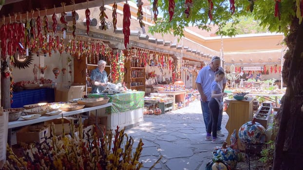 Santa Fe, New Mexico, USA-June 11, 2024-Slow motion-A vibrant outdoor market showcasing an array of colorful ceramics, pottery, and handcrafted items. Shoppers explore the unique local crafts under a sunny sky, surrounded by traditional adobe architecture.