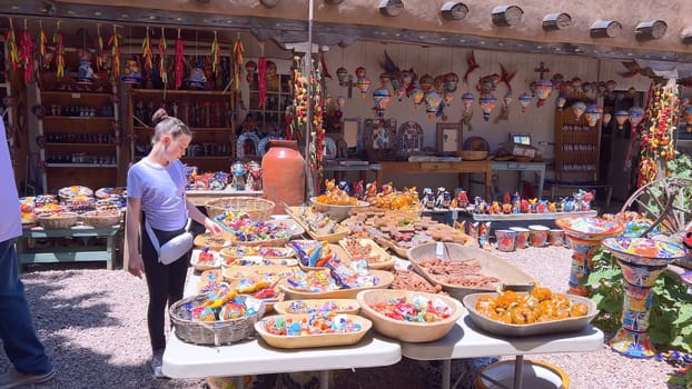 Santa Fe, New Mexico, USA-June 11, 2024-Slow motion-A vibrant outdoor market showcasing an array of colorful ceramics, pottery, and handcrafted items. Shoppers explore the unique local crafts under a sunny sky, surrounded by traditional adobe architecture.