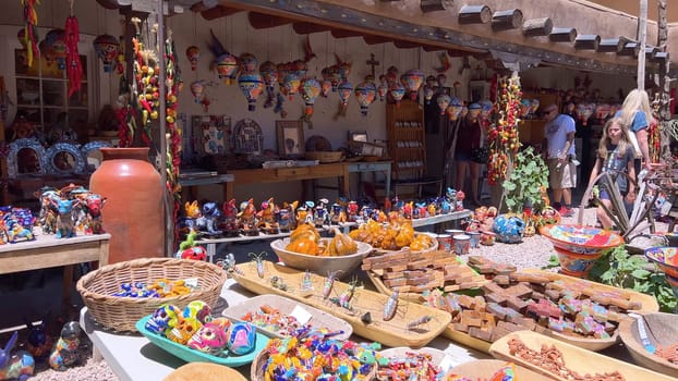 Santa Fe, New Mexico, USA-June 11, 2024-Slow motion-A vibrant outdoor market showcasing an array of colorful ceramics, pottery, and handcrafted items. Shoppers explore the unique local crafts under a sunny sky, surrounded by traditional adobe architecture.