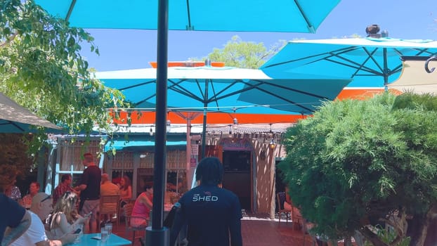 Santa Fe, New Mexico, USA-June 11, 2024-Slow motion-A vibrant outdoor cafe featuring colorful umbrellas providing shade for patrons enjoying their meals on a sunny day. The setting includes lush greenery and a relaxed atmosphere.