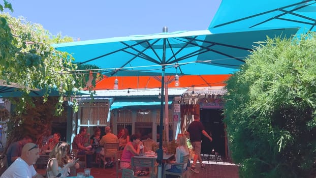 Santa Fe, New Mexico, USA-June 11, 2024-Slow motion-A vibrant outdoor cafe featuring colorful umbrellas providing shade for patrons enjoying their meals on a sunny day. The setting includes lush greenery and a relaxed atmosphere.