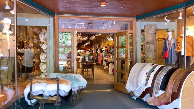 Santa Fe, New Mexico, USA-June 11, 2024-Slow motion-Entrance to a western-themed boutique showcasing hats, furs, and a variety of rustic apparel. The inviting display features wooden doors, mannequins in cowboy attire, and cozy interior decor.