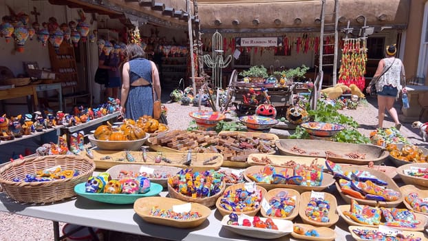 Santa Fe, New Mexico, USA-June 11, 2024-Slow motion-A vibrant outdoor market showcasing an array of colorful ceramics, pottery, and handcrafted items. Shoppers explore the unique local crafts under a sunny sky, surrounded by traditional adobe architecture.