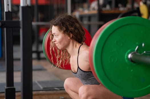Middle-aged woman doing squats with a barbell in the gym