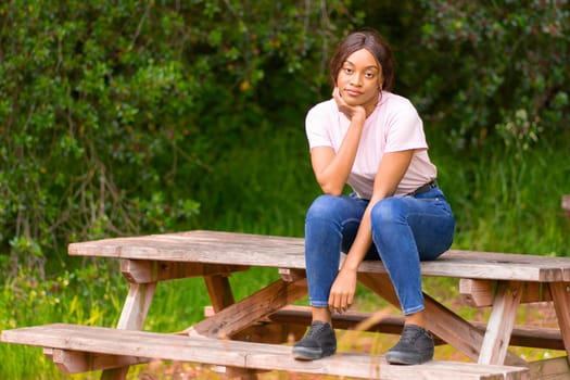 young black woman sitting on a bench in a park on a summer afternoon.