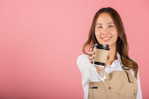 Portrait of Asian happy young woman barista bar tender coffee maker holding coffee tea hot cup studio shot isolated on pink background, female person smiling hold takeaways cup, small business