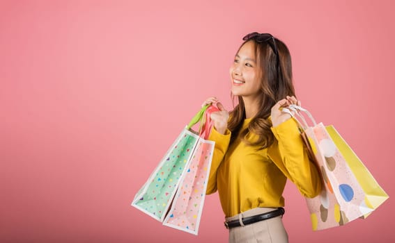 A stylish Asian lady, elegantly holding shopping bags, smiles with joy in a studio portrait on a pink background with copy space. She's the epitome of happy shopping. black friday