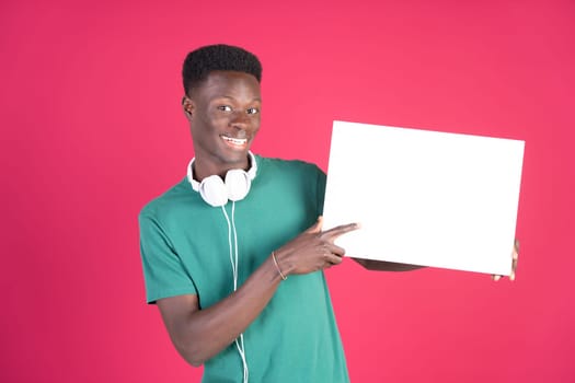 A young man is holding a white sign and pointing to it. He is wearing headphones and a green shirt