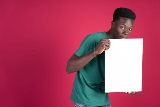 A man in a green shirt is holding a white sign. The sign is blank, and the man is looking at the camera. Concept of curiosity and anticipation, as the man holds the sign and looks at the camera