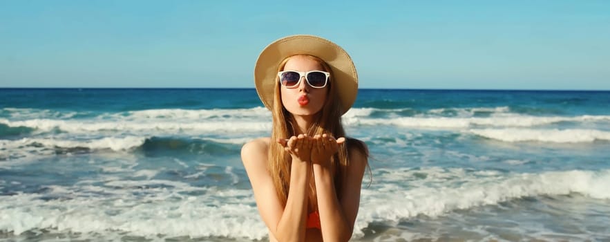 Summer vacation, beautiful happy lovely woman blowing a kiss in bikini swimsuit, tourist straw hat on the beach on sea coast with waves