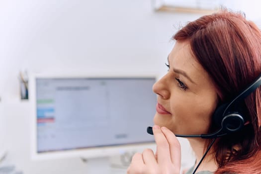 Friendly call center agent answering incoming calls with a headset, providing customer service remotely. Happy woman using her excellent communication skills to resolves customer issues.