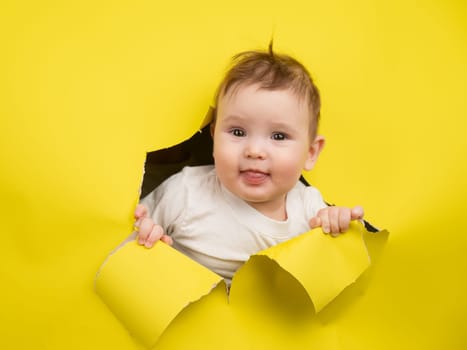 Cute Caucasian baby sticking out of a hole in a paper yellow background