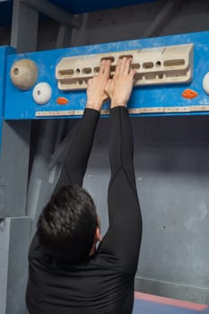 Caucasian man training his fingers on a wooden fingerboard in a rock climbing gym. Vertical photo