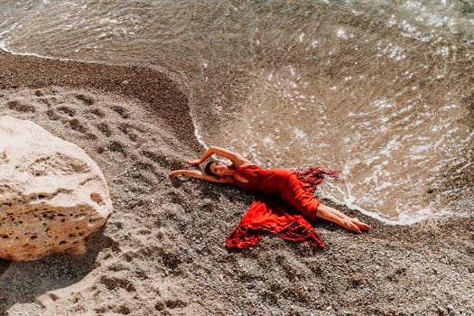 Woman red dress sea. Female dancer in a long red dress posing on a beach with rocks on sunny day.