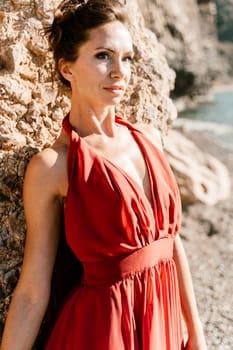 Woman red dress sea. Woman in a long red dress posing on a beach with rocks on sunny day. Girl on the nature on blue sky background