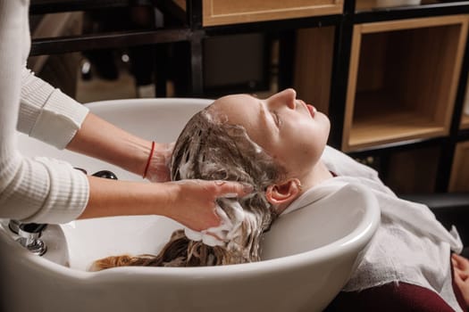 beauty salon master washes client's hair with shampoo for hair care in beauty salon, professional hairdresser,