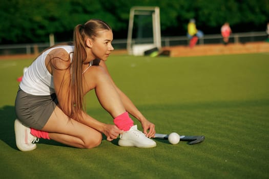 girl hockey player tying sneakers on the field hockey field, concept of playing field hockey, women's sport