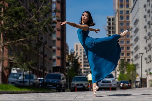 Beautiful Asian ballerina in blue dress dancing outdoors. Urban landscape