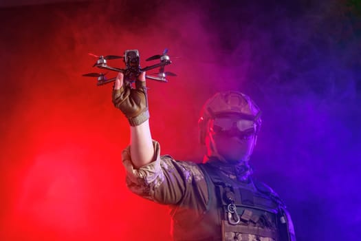 Soldier in gear holds drone against a red and blue smoky background, conveying intensity and military action