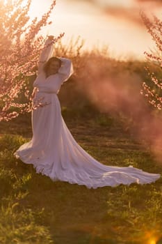 Woman blooming peach orchard. Against the backdrop of a picturesque peach orchard, a woman in a long white dress enjoys a peaceful walk in the park, surrounded by the beauty of nature