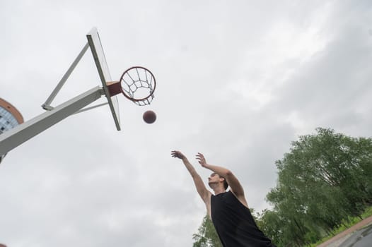 A Caucasian man shoots a ball into a basketball basket outdoors