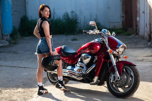 Brunette woman in shorts posing on a red motorcycle