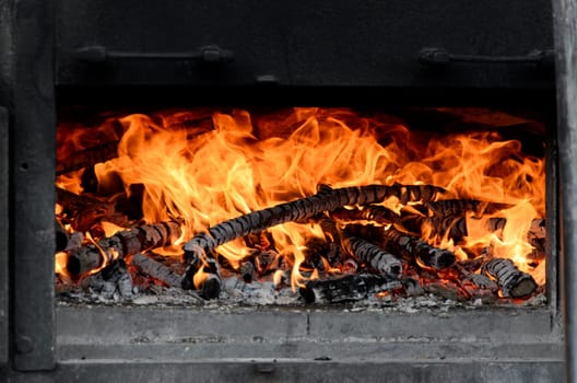 Close-up image of a fireplace filled with burning logs. The fire is framed by the black metal walls of the stove.