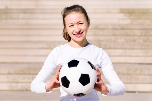 portrait of a smiling sports woman in a concrete soccer court with a ball in her hands, concept of football lifestyle and urban sport in the city