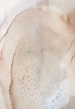 A close-up shot of an abstract ink swirl in soft, muted tones of pink, grey, and white. The ink has a textured, organic quality and creates a visually interesting pattern.