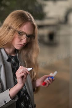 Caucasian woman with glasses writes text in English on a glass wall