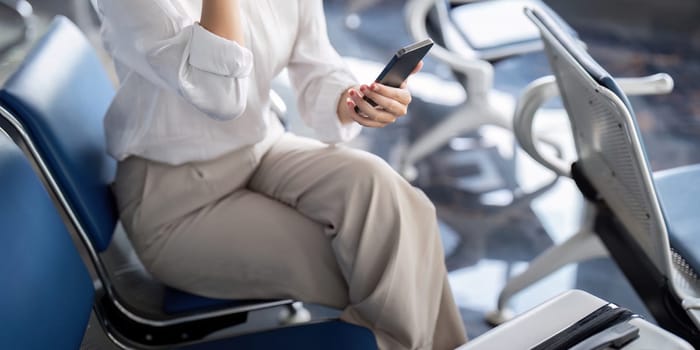 Business professional using smartphone at a modern airport terminal, waiting for a flight. Ideal for travel, business, and technology concepts.