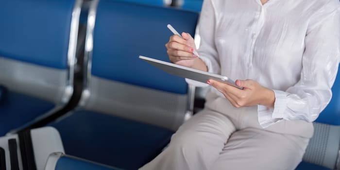 Business professional using a digital tablet while waiting at a modern airport lounge, emphasizing productivity and connectivity.