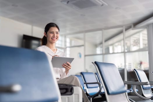 A business professional using a tablet in a modern airport lounge, featuring glass partitions and comfortable seating, ideal for business travel and productivity.