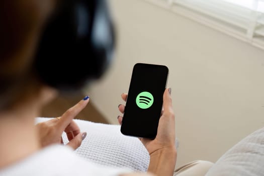 CHIANG MAI, THAILAND - Jun 25, 2024: Person holding a brand new Apple iPhone 14 with Spotify logo on the screen. Spotify is a popular commercial music