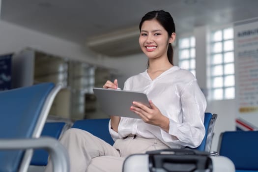 Smiling businesswoman using a tablet while waiting in a modern airport lounge, representing business travel and technology.