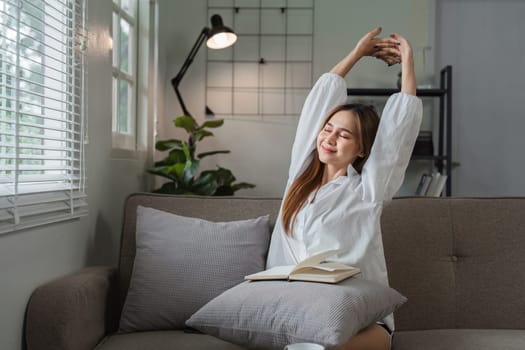 A young woman enjoys a peaceful morning reading a book while sitting on a comfortable sofa in a bright and cozy living room.